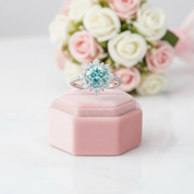 Ring with a blue gemstone on a pink velvet box with flowers in the background