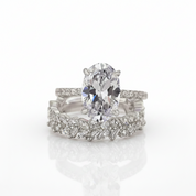 A white gold or platinum engagement ring set with a large oval center stone and matching diamond-accented bands, photographed on a clean white background with a soft reflection below.