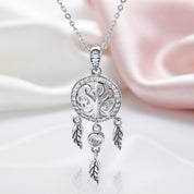 A silver dreamcatcher pendant necklace with clear rhinestones and dangling leaf charms, displayed on a soft white and pink satin background.