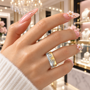 A close-up of a hand wearing a wide silver ring with gold and blue enamel detailing, set against a softly blurred jewelry store background.