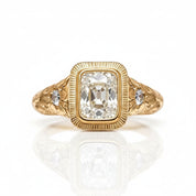 A yellow gold ring featuring a large cushion-cut diamond center stone and two small round diamonds on the shoulders, set against a clean white background with a soft reflection below.