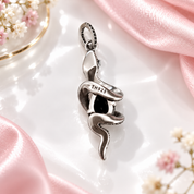 A black snake pendant with a central black gemstone, set in silver-toned metal and detailed with small black stones, shown on a clean white background with a soft reflection below.
