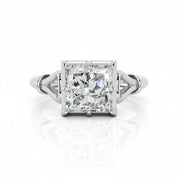 An emerald-cut diamond ring with a silver-toned split-shank band, centered on a reflective white surface.