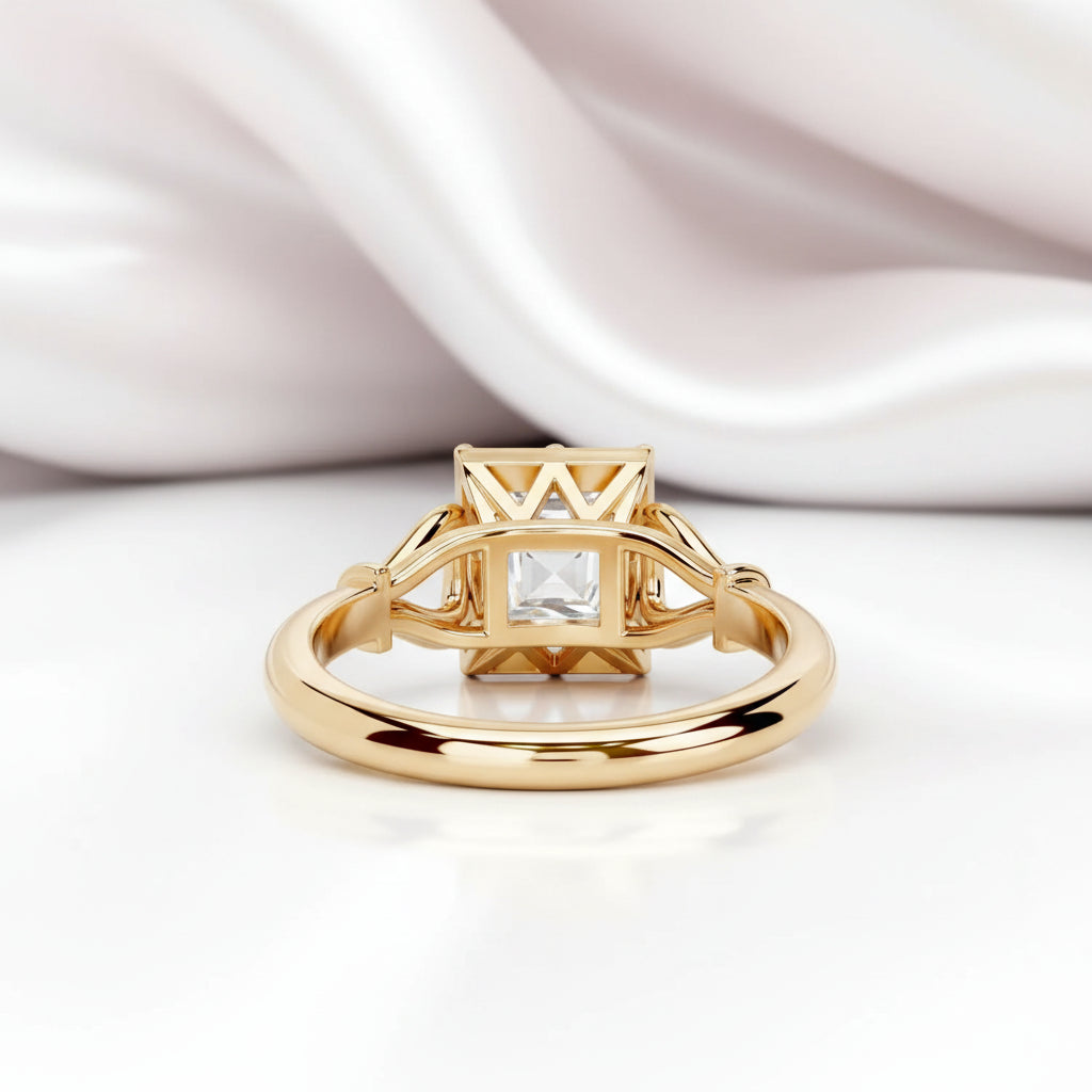 A gold ring with a geometric crown-like setting and a clear square gemstone, photographed on a white surface with soft draped satin fabric in the background.