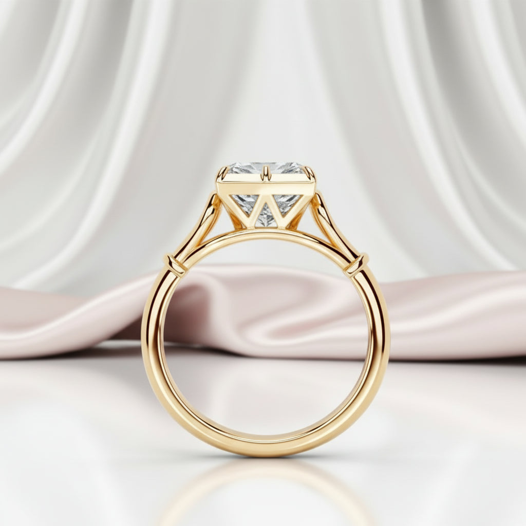 A yellow gold solitaire engagement ring with a large cushion-cut clear gemstone, displayed on a reflective white surface with draped light pink satin fabric in the background.