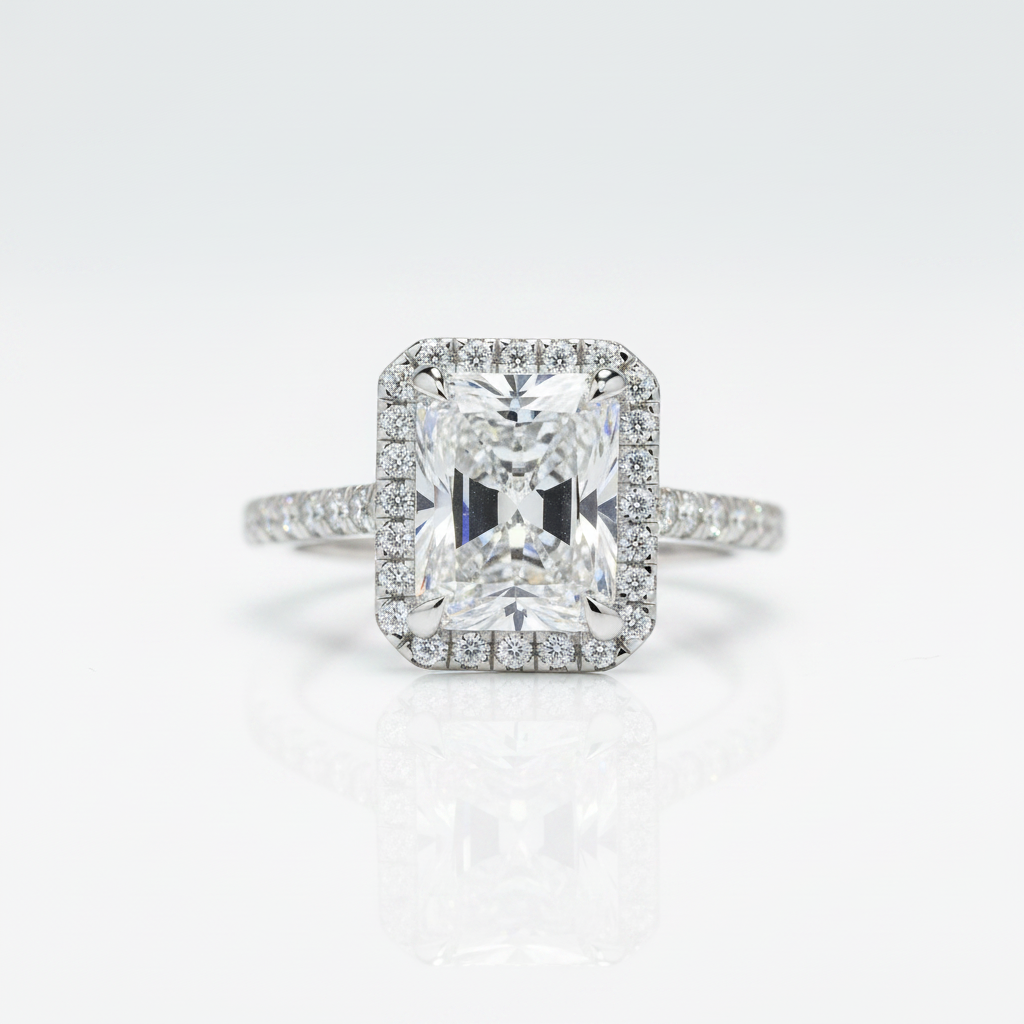 An emerald-cut halo ring featuring a brilliant center stone and a surrounding halo of smaller round stones, set on a slender pavé band, photographed on a clean white background with a soft reflection below.