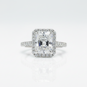 An emerald-cut halo ring featuring a brilliant center stone and a surrounding halo of smaller round stones, set on a slender pavé band, photographed on a clean white background with a soft reflection below.