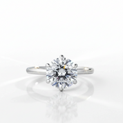 A classic solitaire engagement ring featuring a round brilliant-cut diamond set in a polished white gold or platinum band, shown on a clean white reflective surface.