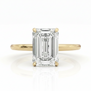 An emerald-cut diamond engagement ring with a yellow gold band, shown on a clean white background with a soft reflection.