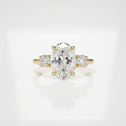 A yellow gold three-stone ring featuring a large oval center diamond flanked by two round side diamonds, set against a clean white background with a soft reflection.