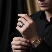 Close-up of a person wearing a gold watch and a ring with a green gemstone.