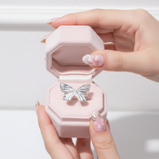 Pink jewelry box with butterfly design held by a hand on a light background