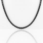 A black beaded tennis necklace with faceted round beads, displayed against a clean white background with a soft reflection below.