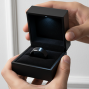 Black ring in an open black box held by hands against a neutral background