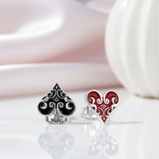 Black spade and red heart earrings on a reflective surface with a blurred background