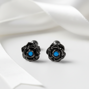 Black rose-shaped cufflinks with blue centers on a white fabric background