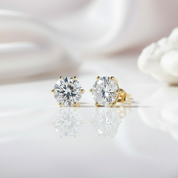 Gold stud earrings with clear gemstones on a reflective surface