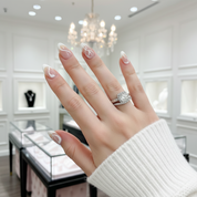 Hand wearing a diamond ring with a blurred jewelry store background