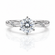 A silver-toned solitaire engagement ring with a round brilliant-cut center stone and small accent stones on the band, shown on a clean white background with a soft reflection below.