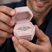 A close-up of a man holding an open hexagonal pink ring box that displays a silver-toned solitaire engagement ring with a clear round gemstone.