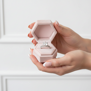 Hand holding a pink hexagonal ring box with a diamond ring inside against a white background