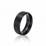 A matte black titanium ring with a satin finish and a polished beveled edge, shown on a reflective white surface. The inside of the band is engraved with the word 'TITANIUM'.