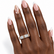 A close-up of a hand with manicured nails wearing a rose gold ring with clear gemstones on the ring finger, set against a plain white background.
