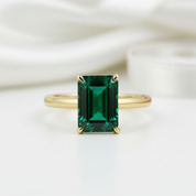 Gold ring with a green emerald-cut gemstone on a white background