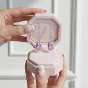 Pink diamond earrings in a hexagonal pink box held by a hand with decorative nails.