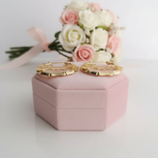Gold hoop earrings on a pink jewelry box with flowers in the background