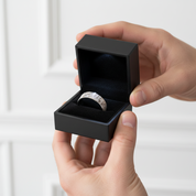 Person holding a black jewelry box with a silver ring inside against a white background