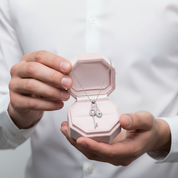 Person holding a pink jewelry box with a necklace inside, wearing a white shirt.