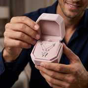 A close-up of a man holding an open pink jewelry box that displays a silver butterfly necklace with small clear stones.