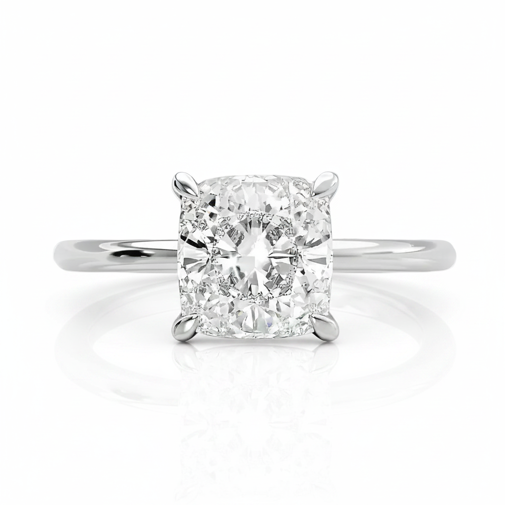 A radiant cut diamond solitaire engagement ring in a four-prong white gold or platinum band, centered on a clean white background with a soft reflection below.