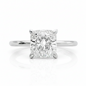 A radiant cut diamond solitaire engagement ring in a four-prong white gold or platinum band, centered on a clean white background with a soft reflection below.