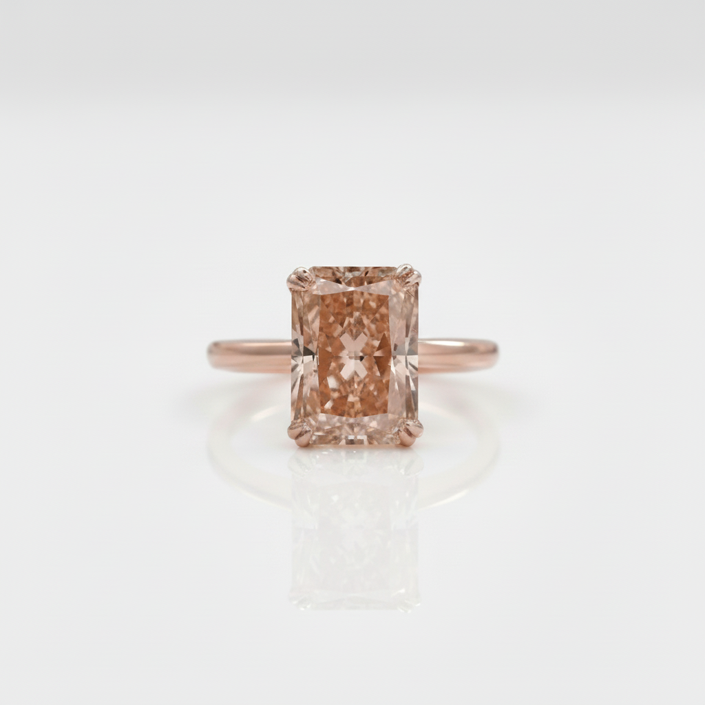 An emerald-cut peach diamond ring set on a rose gold band, centered against a clean white background with a soft reflection below.