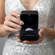 Person holding a black jewelry box with a silver ring inside, wearing a sparkly outfit.