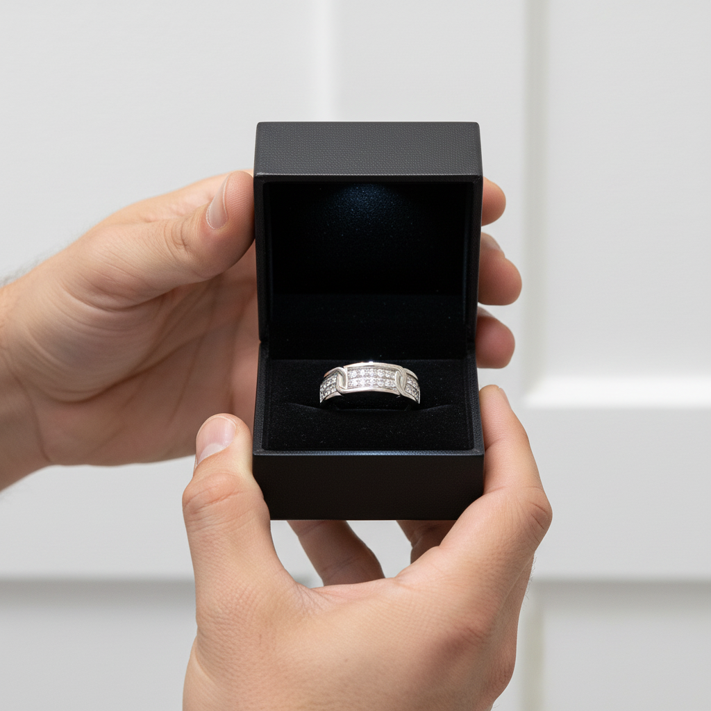 Hand holding a black jewelry box with a silver ring inside against a white background