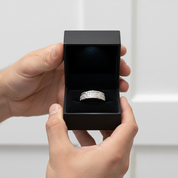 Hand holding a black jewelry box with a silver ring inside against a white background