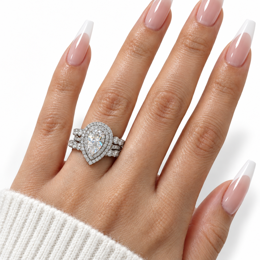 A close-up of a hand with long, glossy nude-and-white manicured nails wearing an oval silver-toned ring set with a large pear-shaped clear center stone and smaller surrounding stones.
