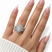A close-up of a hand with long, glossy nude-and-white manicured nails wearing an oval silver-toned ring set with a large pear-shaped clear center stone and smaller surrounding stones.