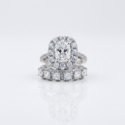 A silver-toned diamond ring set featuring a cushion-cut center stone surrounded by a halo, with a matching pavé band ring underneath, photographed on a clean white reflective surface.