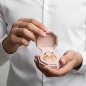 Person holding a pink jewelry box with gold earrings inside against a white background