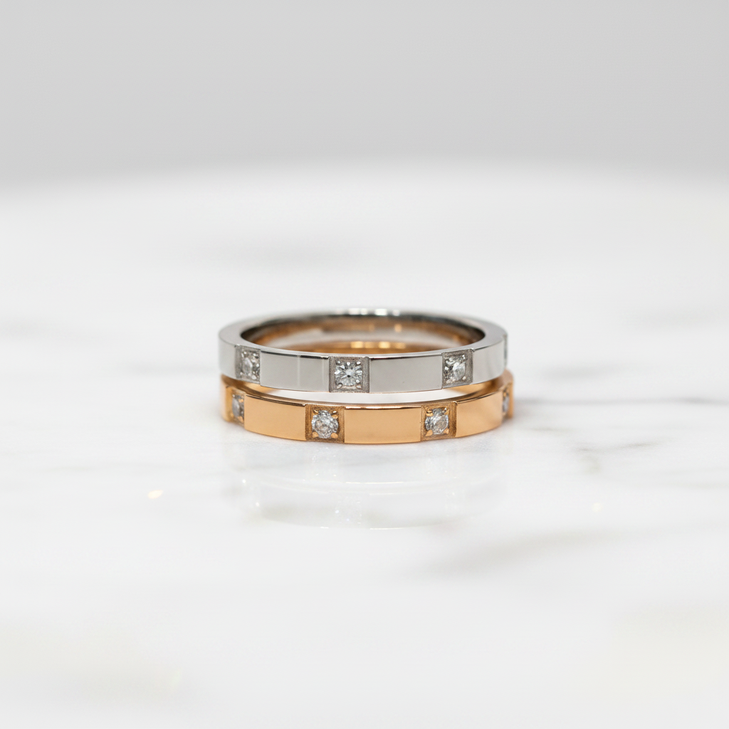 A two-tone ring set featuring a silver band and a rose gold band, both adorned with small square-cut diamonds, displayed on a white marble surface.