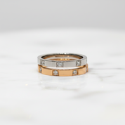 A two-tone ring set featuring a silver band and a rose gold band, both adorned with small square-cut diamonds, displayed on a white marble surface.