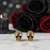 Gold skull-shaped earrings on a marble surface with black and red roses in the background.