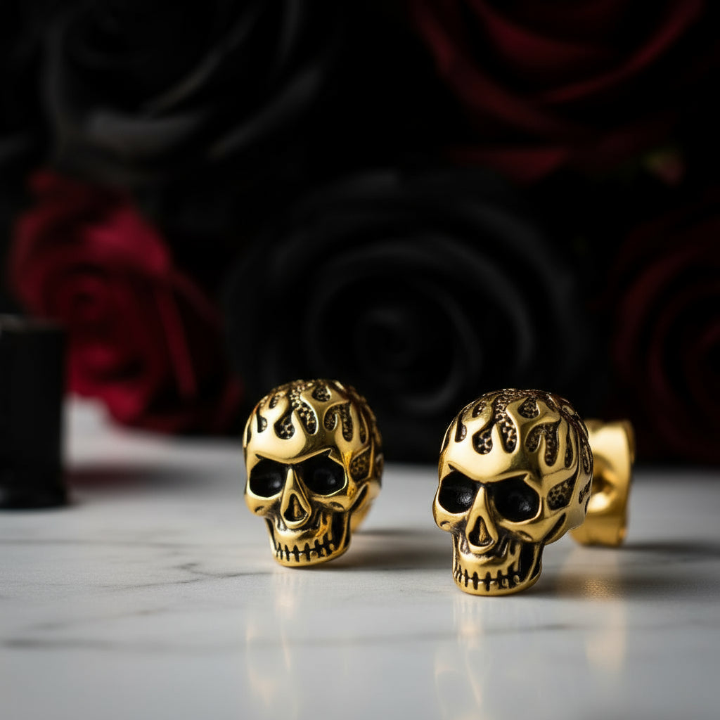 Gold skull-shaped earrings on a reflective surface with a dark floral background