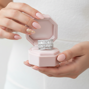 Pink jewelry box with two rings inside, held by a person with pink nail polish.