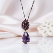 Jewelry necklace with purple teardrop pendant and red gemstones on a soft background