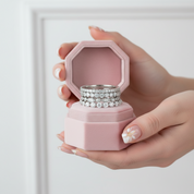 Hand holding a pink jewelry box with three silver rings inside against a white background